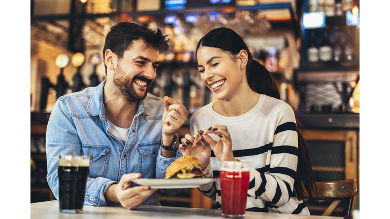 Young couple eating burgers and drinking beer