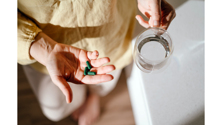 A woman standing at a table with green pills in her hand