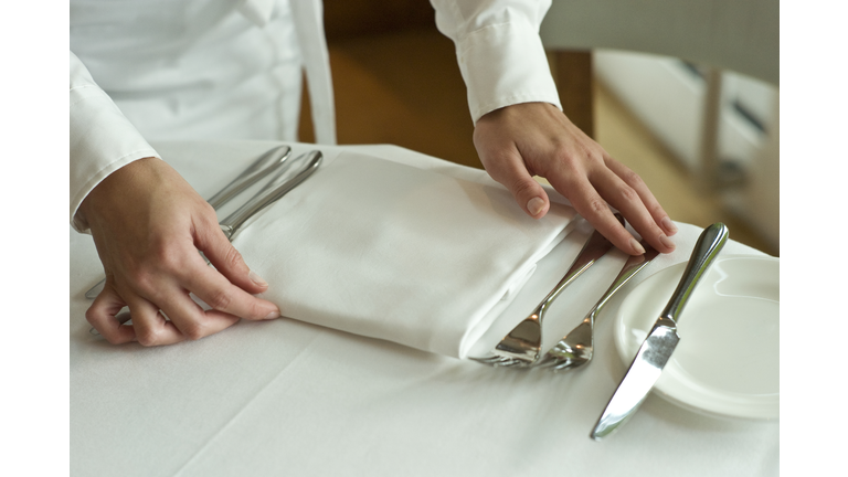 Waitress adjusting table settings in restaurant, mid section