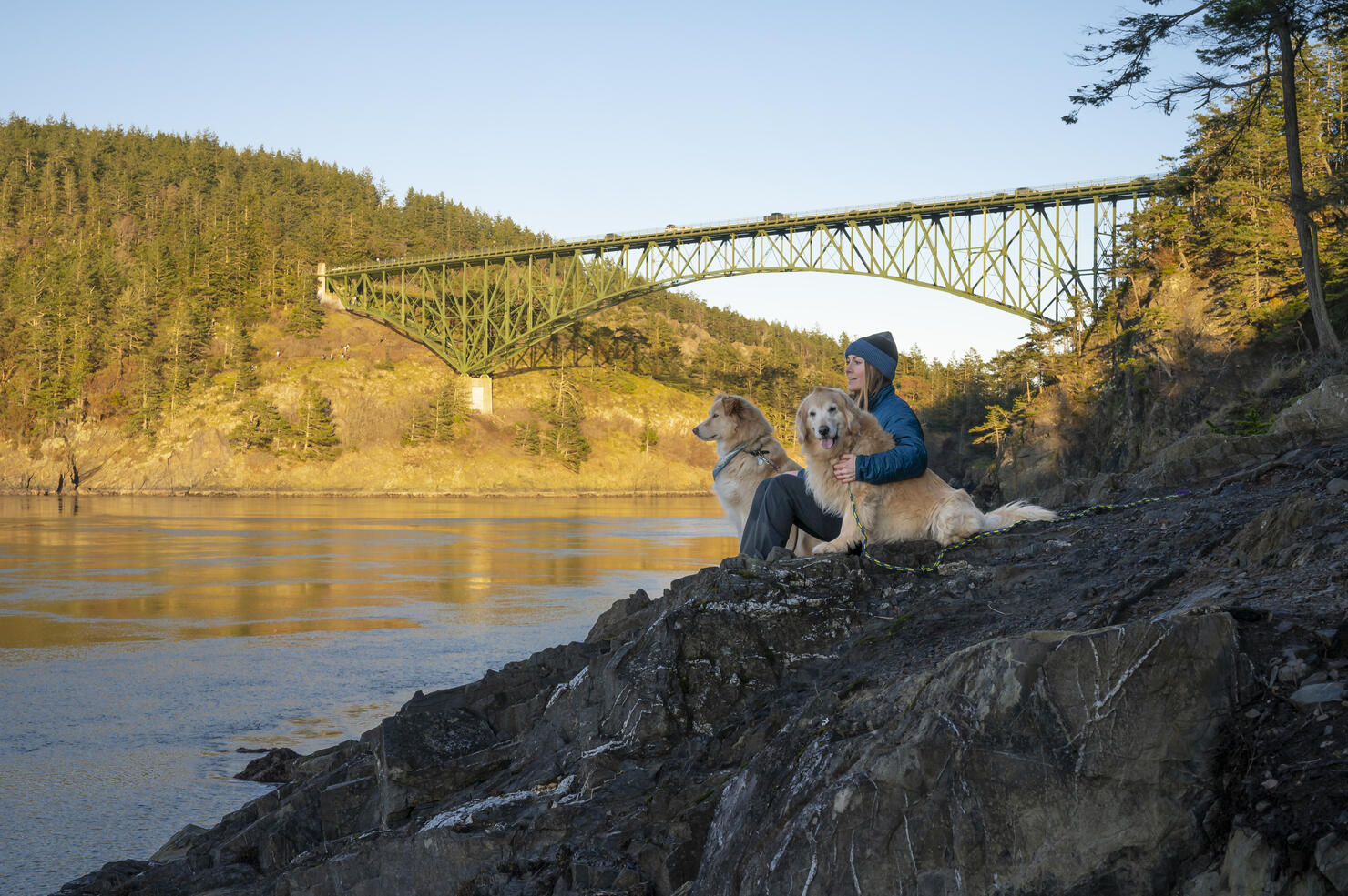 Happy female sitting with dogs on a cliff at Deception Pass