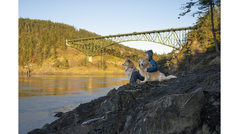 Happy female sitting with dogs on a cliff at Deception Pass