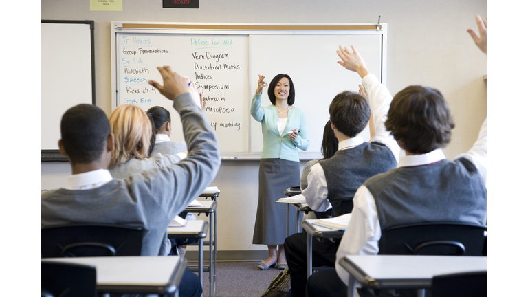 School children (14-18) raising hands in class