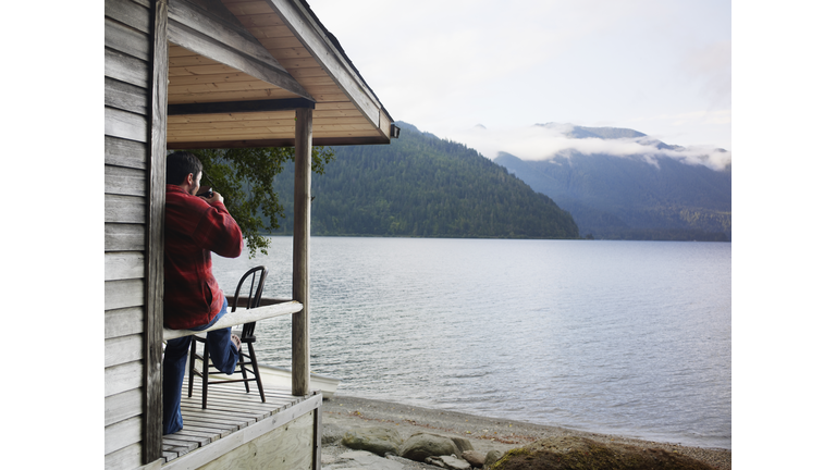 Man drinking coffee on front porch of lake cabin