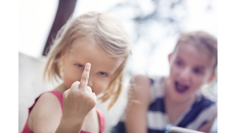 Girl holding up a middle finger, with shocked sibling in the background