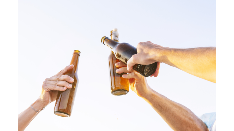 Three people doing celebratory toast with beer bottles on beach at sunset, Oliva, Valencia, Spain. - stock photo