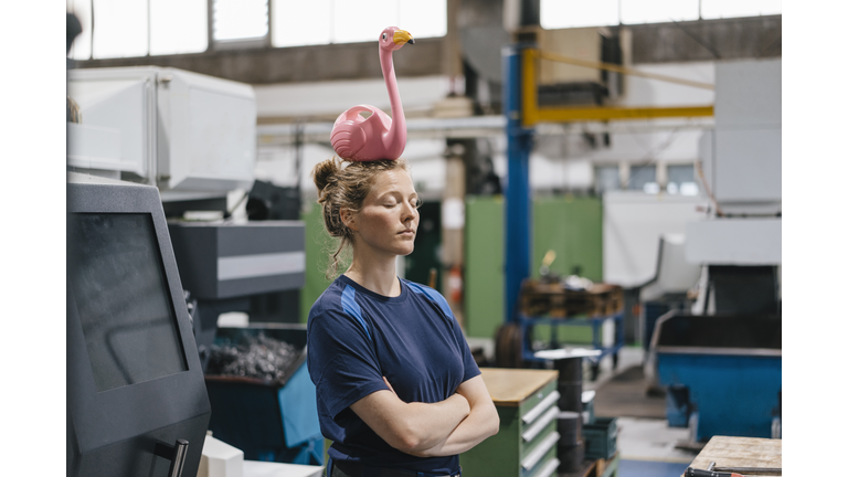 Young woman working as a skilled worker in a high tech company, balancing a pink flamingo on her head