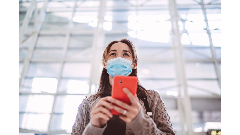 Young asian lady in medical face mask using smartphone joyfully in train station