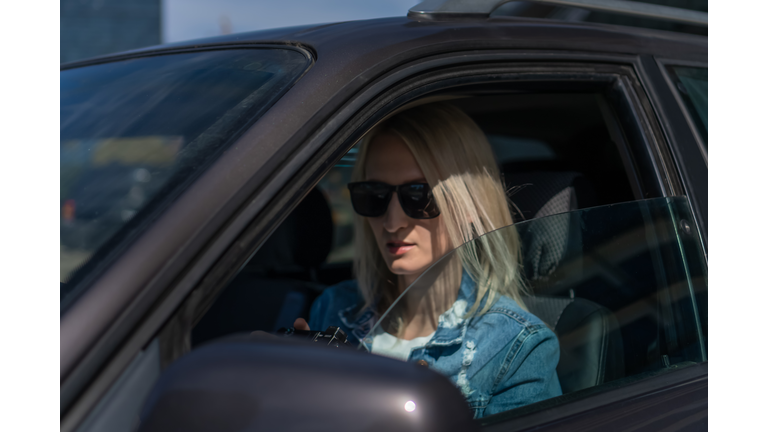 Woman in sunglasses with a camera sits in a car and takes pictures with a professional camera, a private detective or a paparazzi spy. Journalist is looking for sensations and follows celebrities.