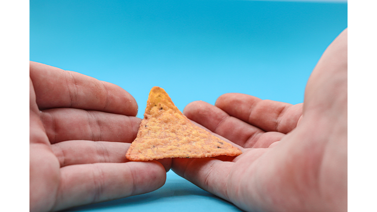 hands holding triangle doritos or nachos, on blue background, ideal copy space