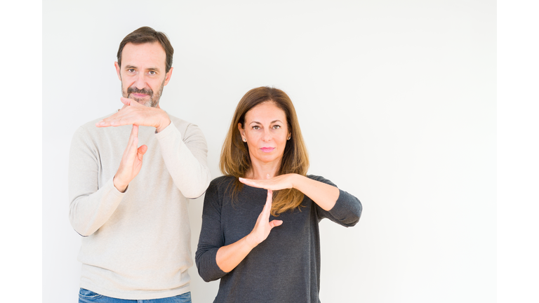 Beautiful middle age couple in love over isolated background Doing time out gesture with hands, frustrated and serious face