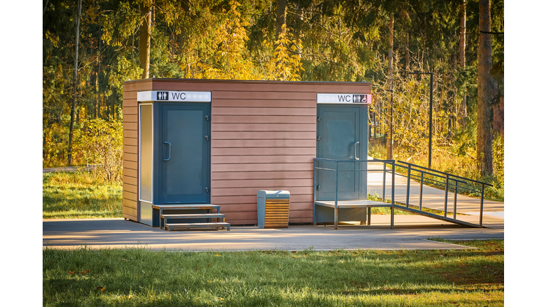 Public toilet in park. Wooden WC building in fall forest in park. Modern outdoor public toilet in city park.