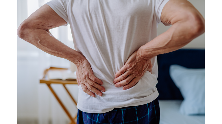 Senior man having back pain, standing in his bedroom.