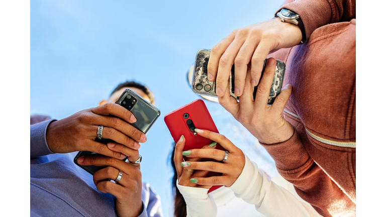 Low angle view of three young people using mobile phones outdoors