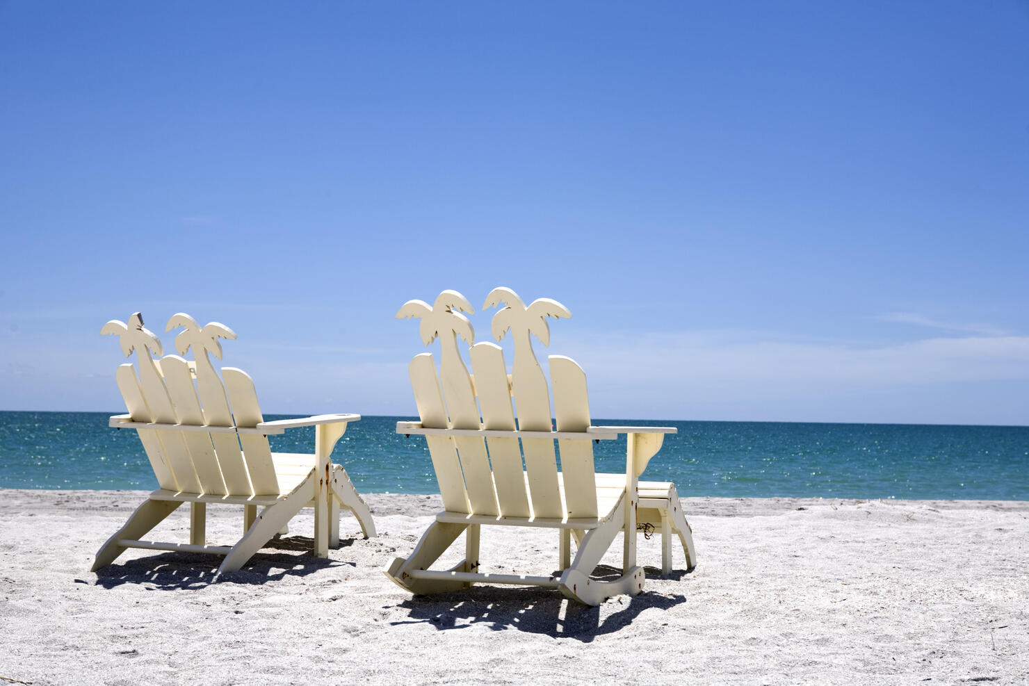 Back of two white wooden chairs on sand with ocean