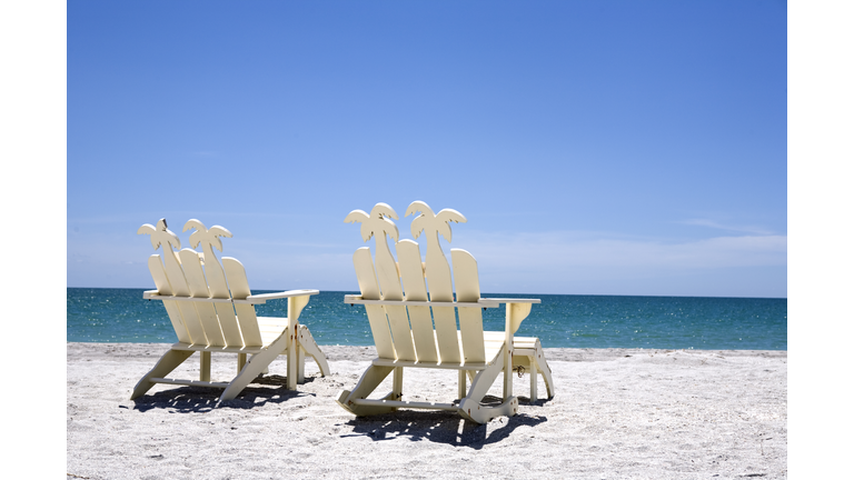 Back of two white wooden chairs on sand with ocean