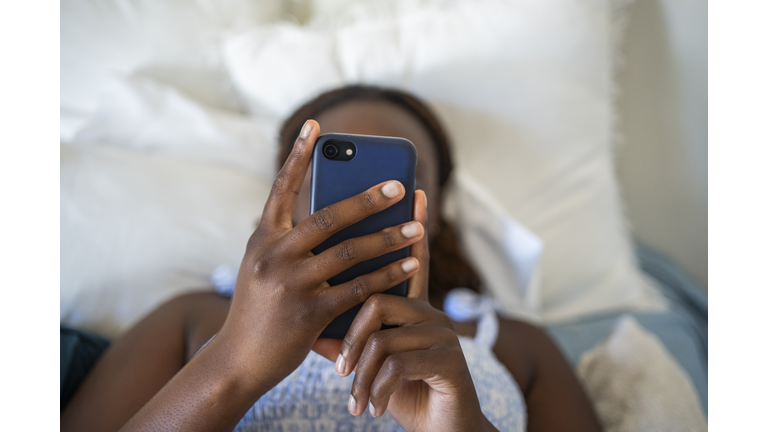 Teenage girl using a phone while lying on her bed