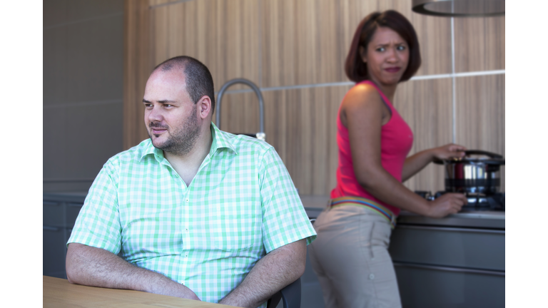 man sitting at kitchen table and woman is cooking