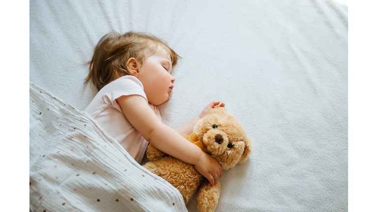 Little baby sleeping on bed embracing soft toy, free space