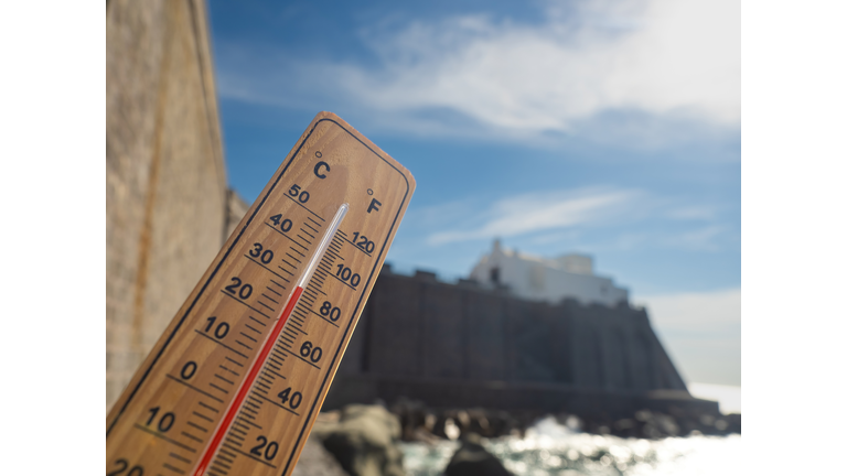 Wooden thermometer showing high temperatures on sunny day.