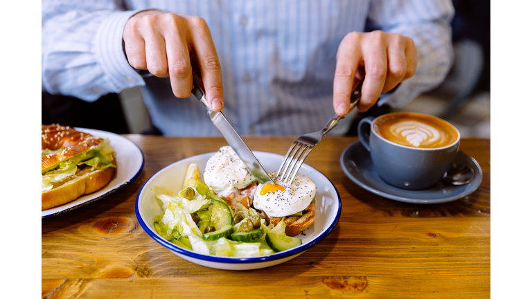 Man eating breakfast with poached eggs, fresh salad and coffee
