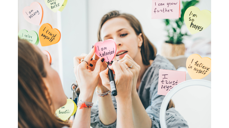 Woman writing affirmations on a sticker near the mirror.