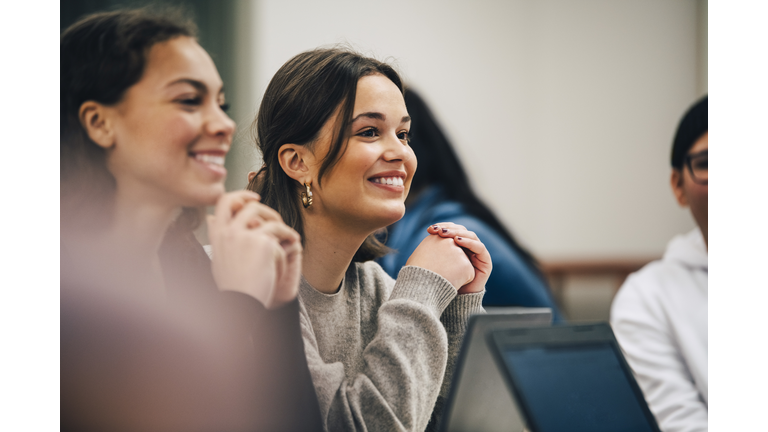 Smiling female students looking away while sitting in classroom