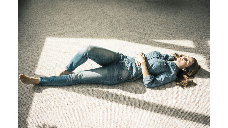 Young woman lying on carpet in the living room enjoying sunlight