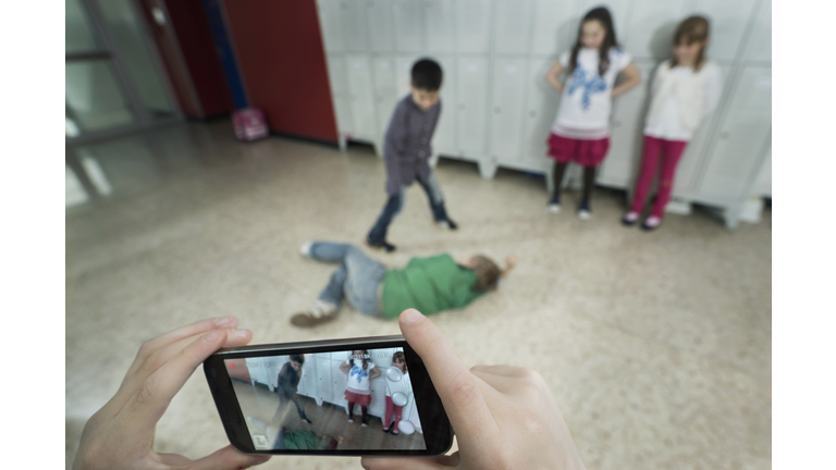 Persons hand filming two schoolboys fighting in school corridor with mobile phone, Bavaria, Germany