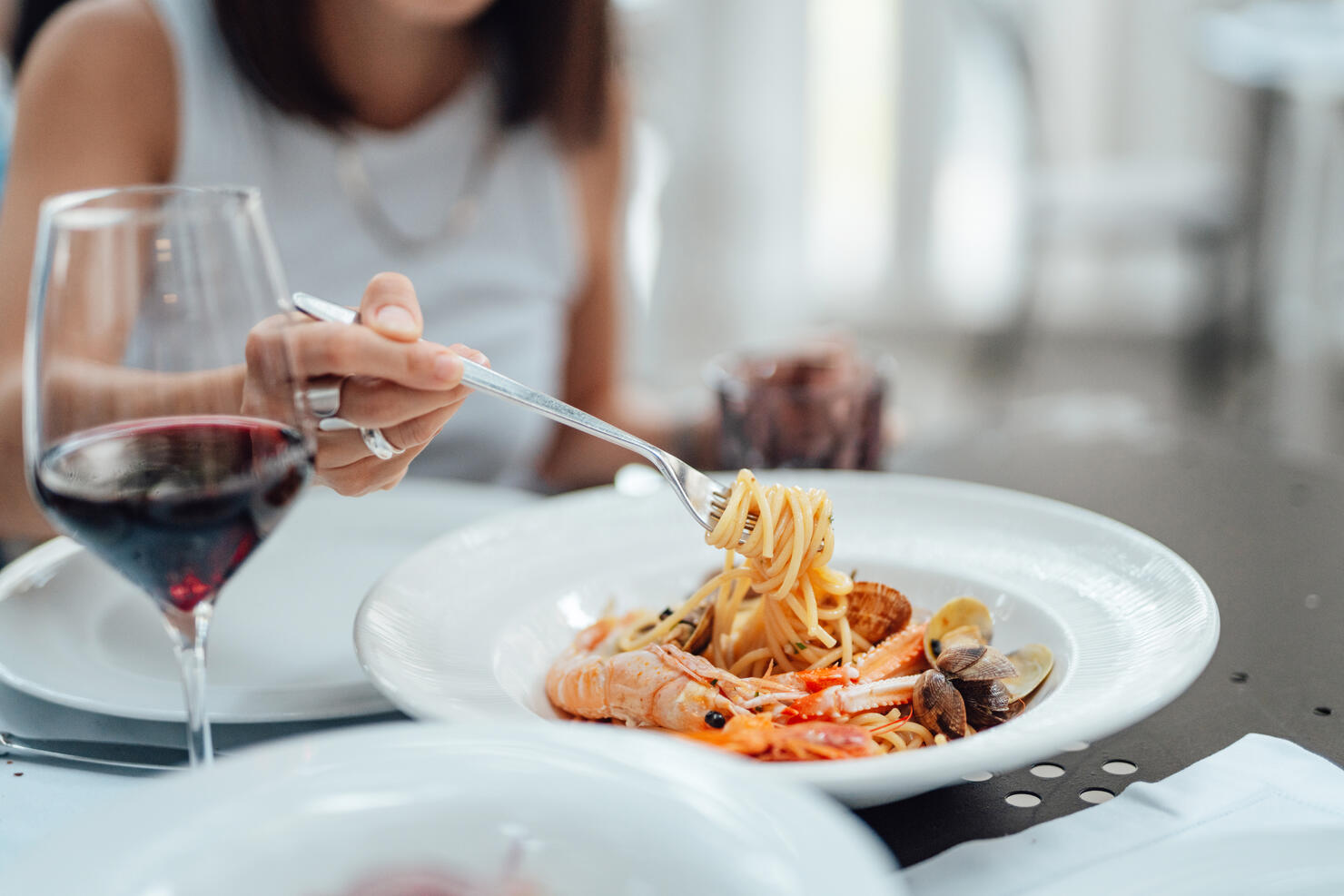 Close-up of young woman eating fresh seafood pasta in restaurant