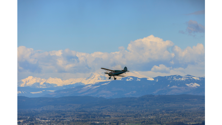 Silhouetted bi-plane flying above snow capped mountainous landscape