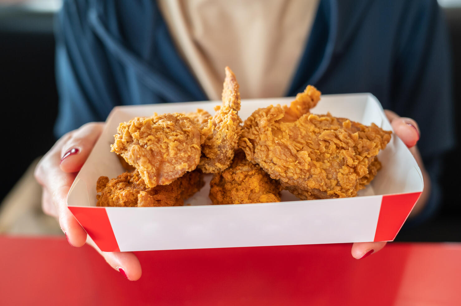 Cropped shot of woman holding a paper box with pieces of fried chicken before eating.