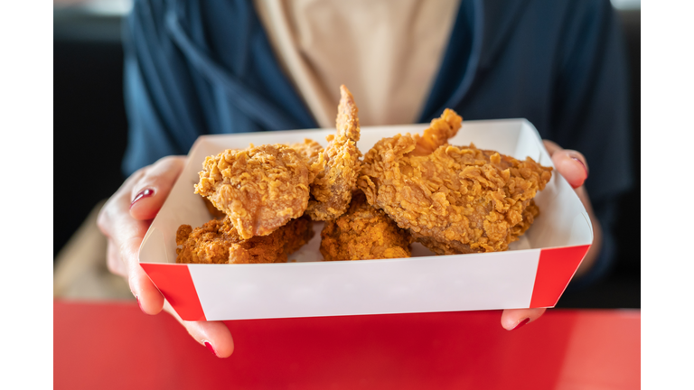 Cropped shot of woman holding a paper box with pieces of fried chicken before eating.