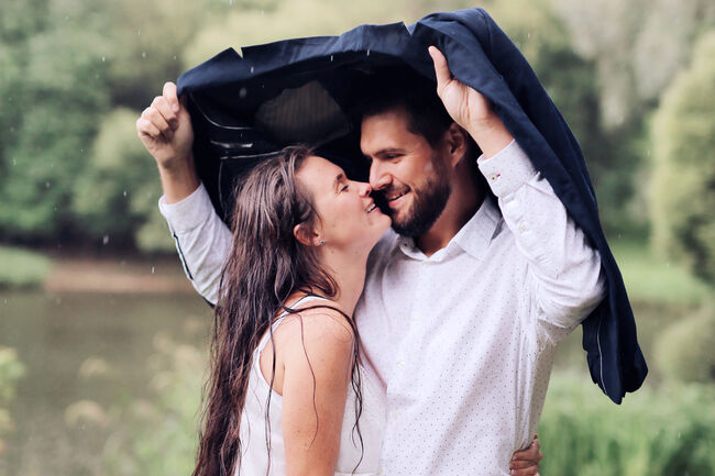 A beautiful young couple in love kissing in the rain in a summer park