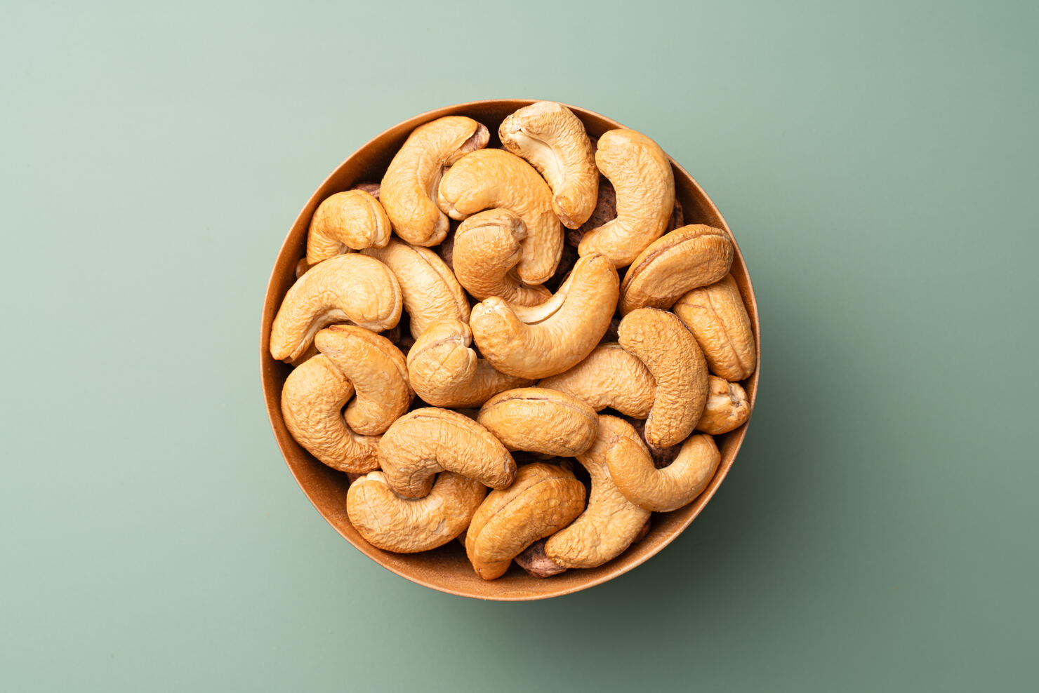Cashew Nuts in Wooden Bowl on Green Background