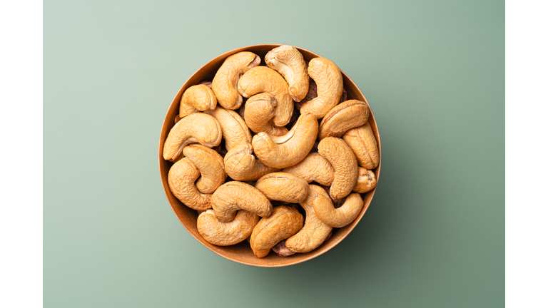 Cashew Nuts in Wooden Bowl on Green Background