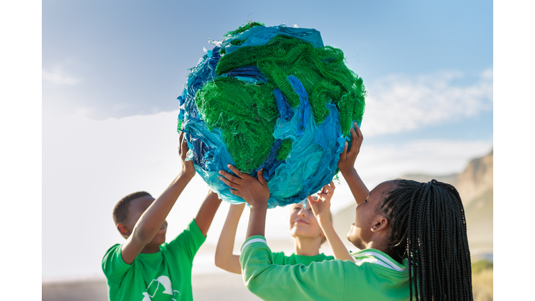 Group of young climate activists holding up a globe together by the sea