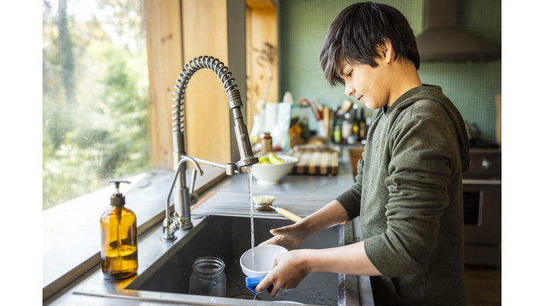 Teenage boy washing dishes in kitchen