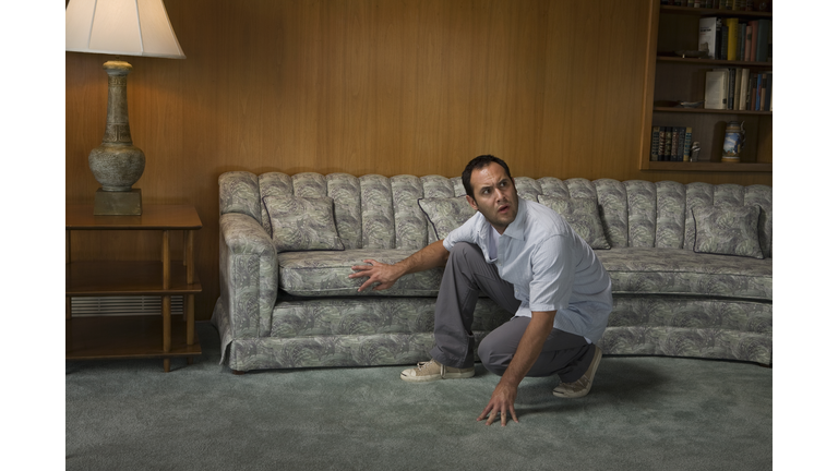 Scared man crouching in front of sofa