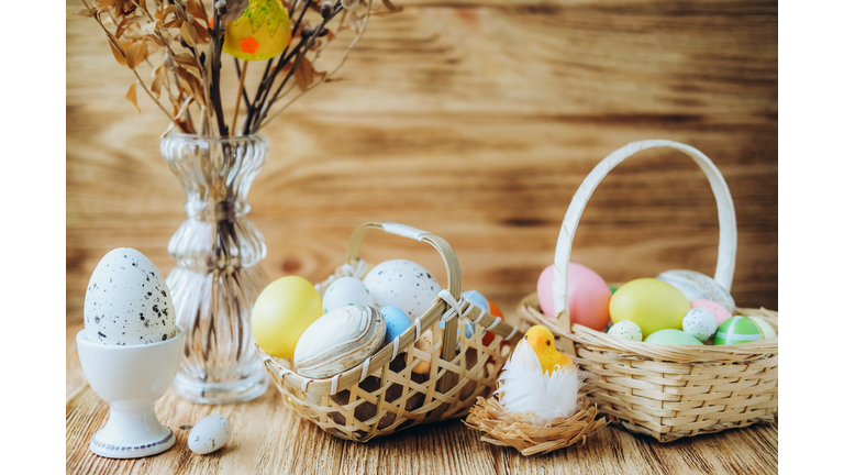 An egg in a cup beside a vase with plants, baskets with eggs and a toy chick in a nest.