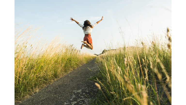 Enthusiastic young woman jumping on path in field