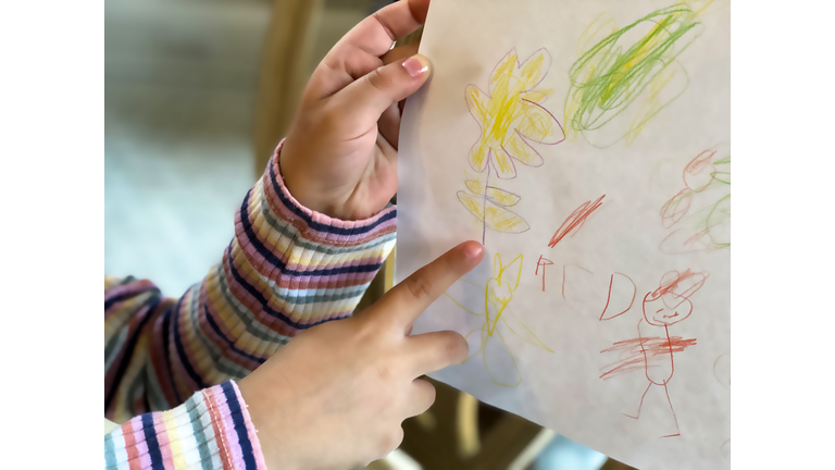 mixed-race young girl points to a yellow flower on her art drawing