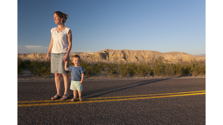 Mother and toddler son walking together on paved road through desert