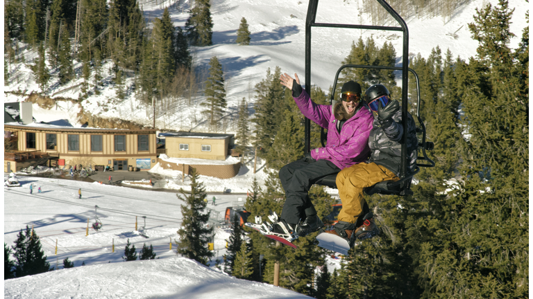 Two Snowboarders in Full Winter Gear Ride the Ski Lift and Wave at the Camera at Eldora Ski Resort near Boulder, Colorado on a Bright, Sunny Day in Winter