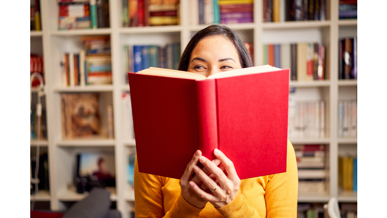 Female young behind book with face covered for a red book while smiling