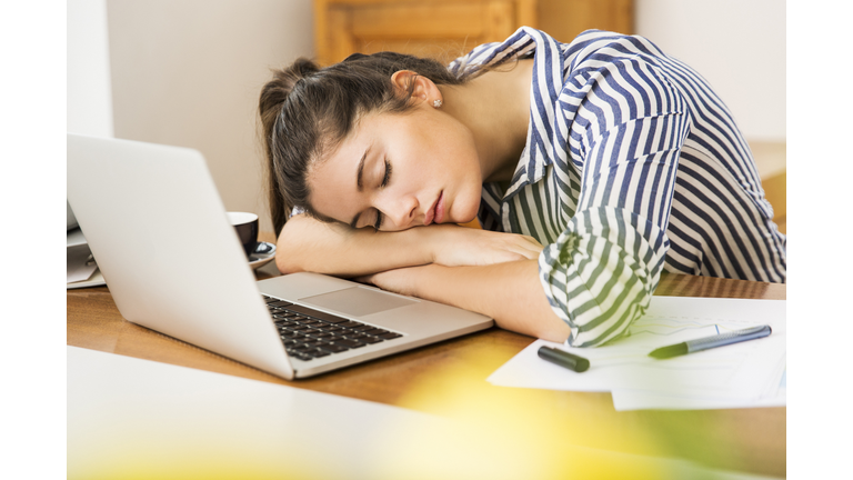 Young woman sleeping in front of her laptop at home