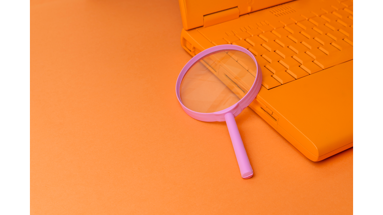 Orange Laptop And Pink Magnifying Glass On Orange Background