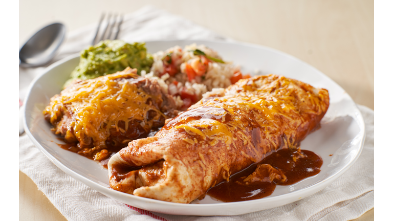 mexican wet burrtio platter with red enchilada sauce, refried beans, rice and guacamole