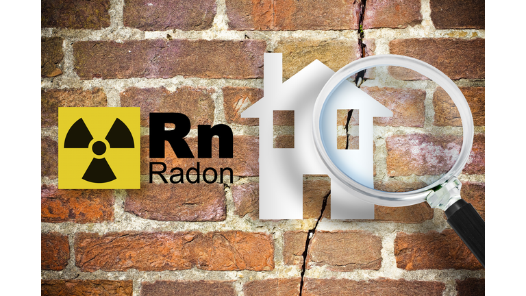 The danger of radon gas in our homes - concept with periodic table of the elements, radioactive warning symbol and home silhouette seen through a magnifying glass against a cracked brick wal