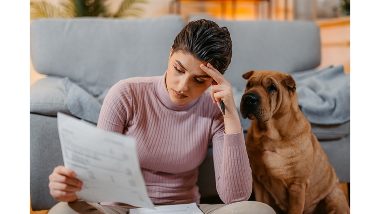 Young Woman With Her Dog Checking Her Finances At Home