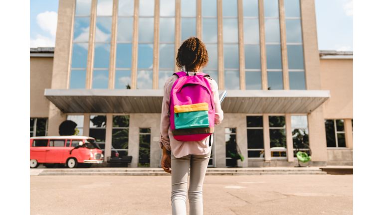 Small African-American kid schoolchild pupil student going to school, standing at the school yard before classes lessons. New academic year semester. Welcome back to school!